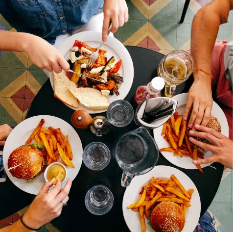 People sharing burgers, fries, and salad around a table