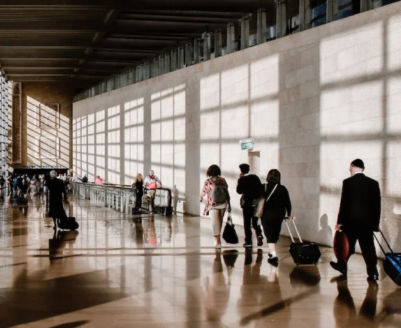 Travelers walking through a bright airport terminal with luggage